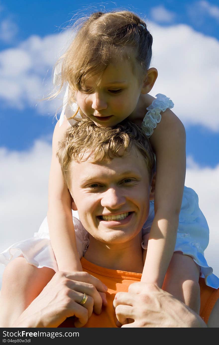 The father holds the daughter on his shoulders, in nature