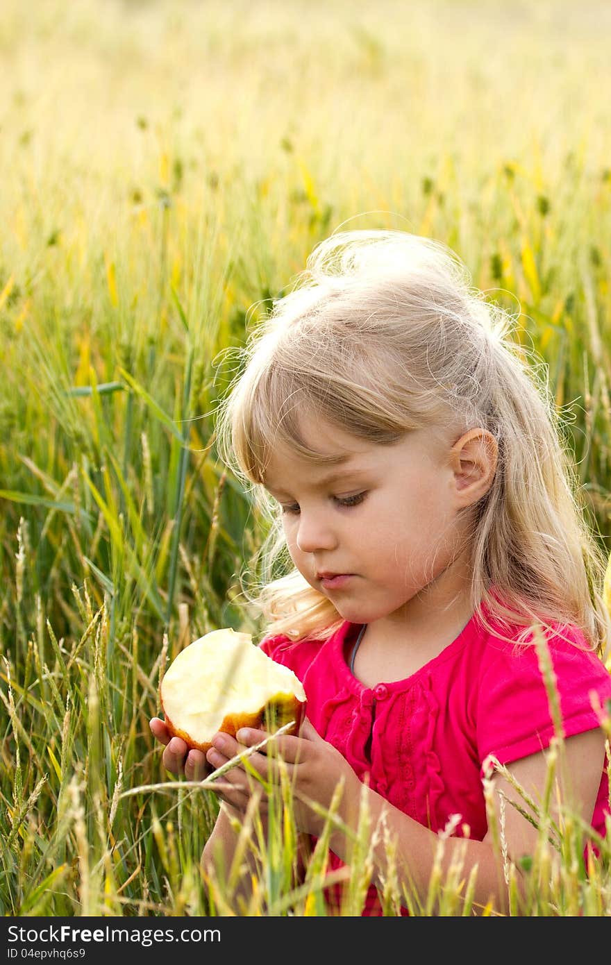 Beautiful serious girl biting an apple in a wheat field. Beautiful serious girl biting an apple in a wheat field