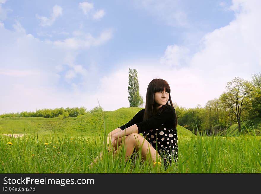 Girl sitting on green grass with blue sky and clouds. Girl sitting on green grass with blue sky and clouds