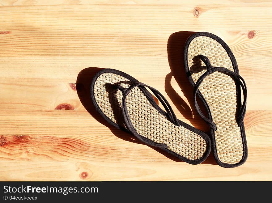 Pair of female flip-flops on wooden floor under sunbeam