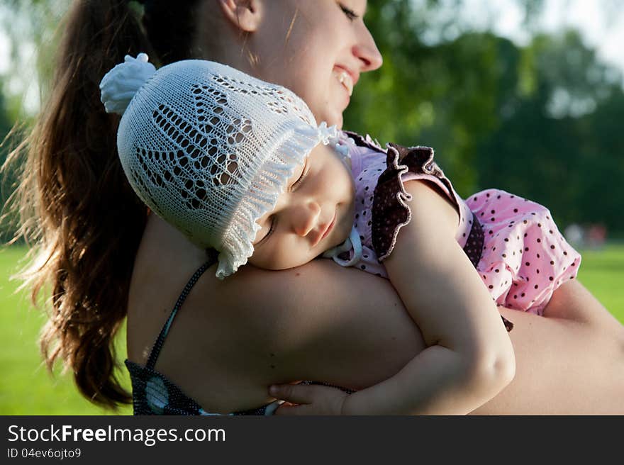 Woman holds child on shoulder in the park