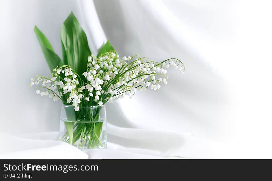 Lily of the valley in glass vase on white textile background with free space for text