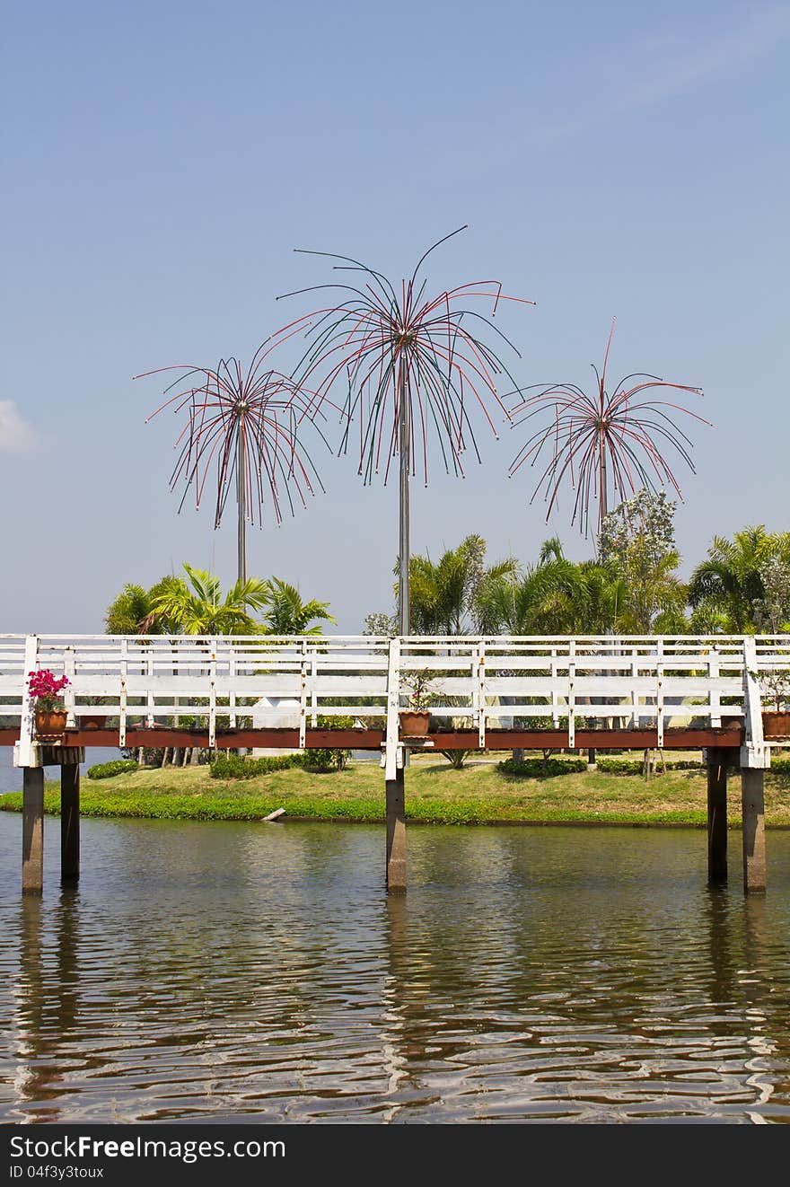 White wooden bridge on the water with poles decorated with coconut trees on a mound. White wooden bridge on the water with poles decorated with coconut trees on a mound.