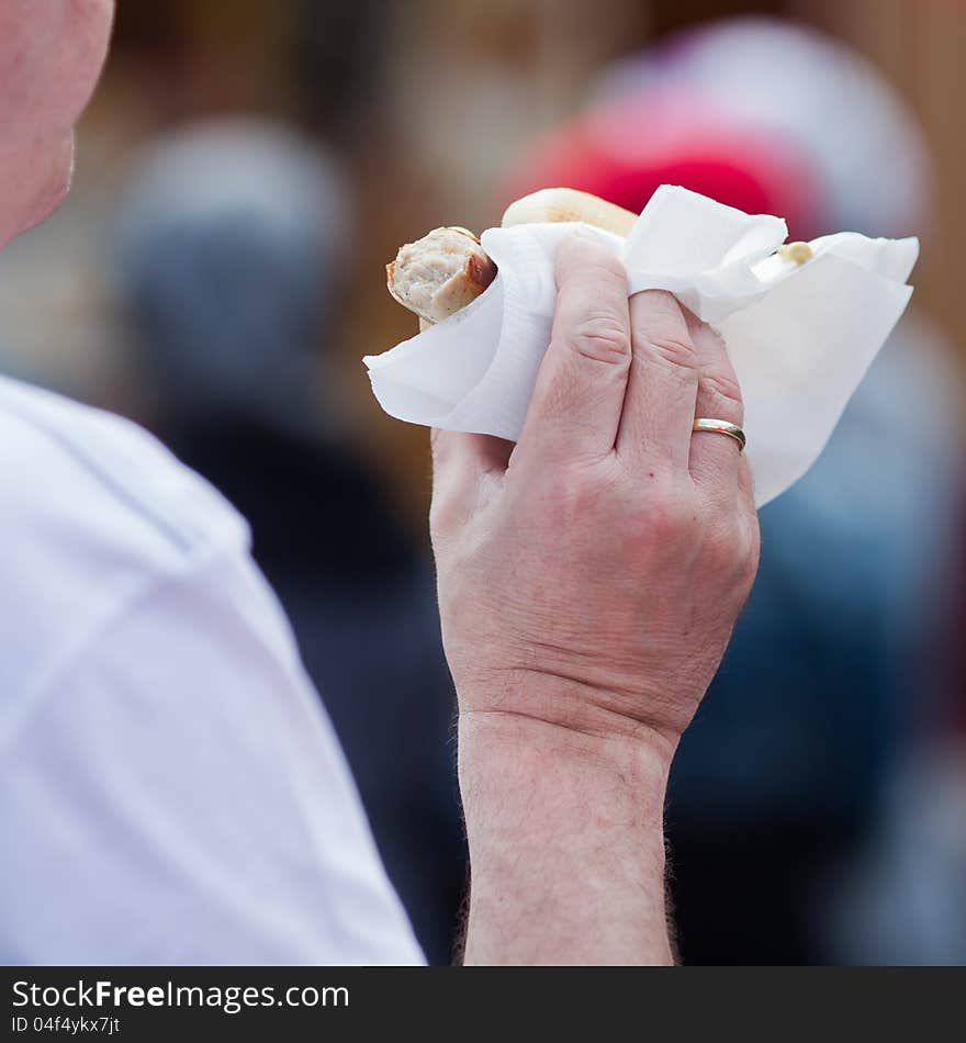 The hand of an unrecognizable man holds a bratwurst with vignette in his hand. A piece of the wurst is already bitten off. The hand of an unrecognizable man holds a bratwurst with vignette in his hand. A piece of the wurst is already bitten off