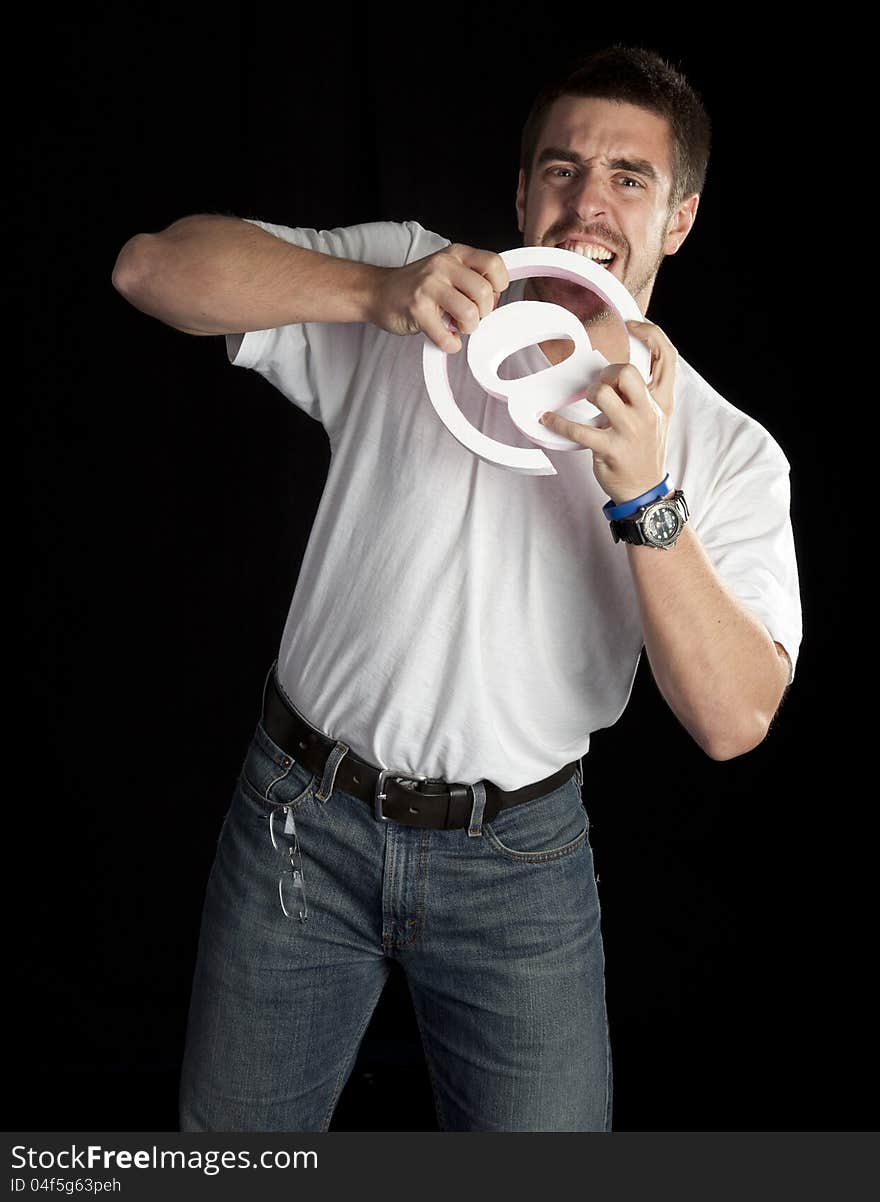 Young angry man bites and email symbol isolated on black in studio. Young angry man bites and email symbol isolated on black in studio