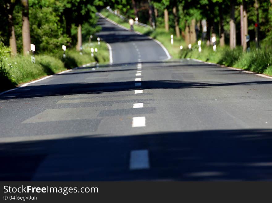 A road in summer wide with a bicyclist riding up a hill far away in the distance. A road in summer wide with a bicyclist riding up a hill far away in the distance