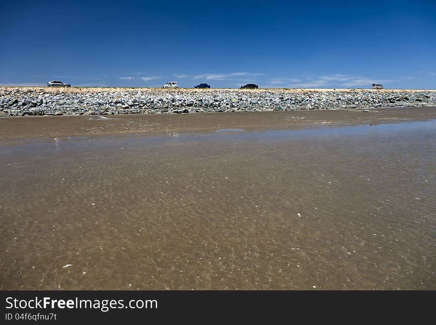 Cars running on a dam by a beach. Cars running on a dam by a beach.