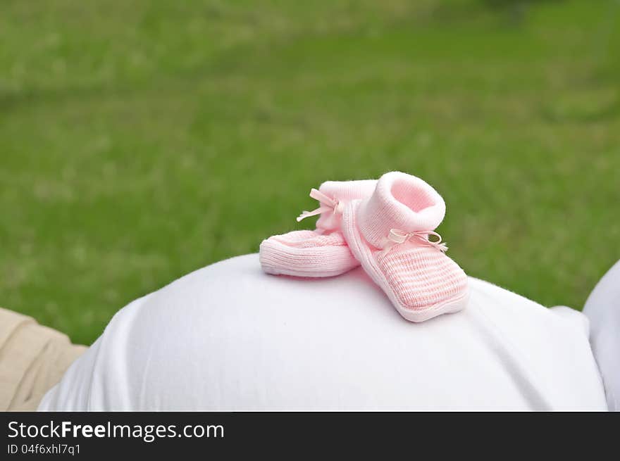 Pink shoes on a pregnant womans belly with a green background. Pink shoes on a pregnant womans belly with a green background