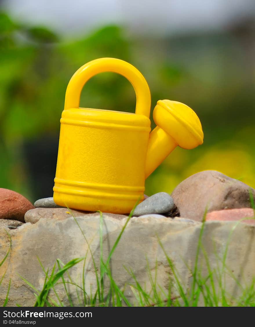 A kids’ watering can on stones in the garden. A kids’ watering can on stones in the garden