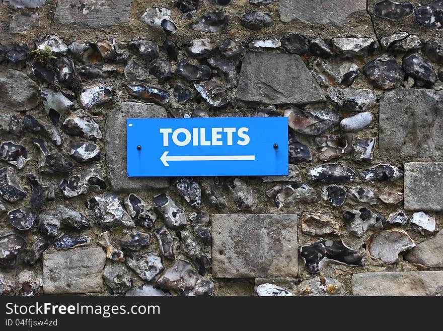 Blue outdoor toilet sign fixed to a flint wall. Blue outdoor toilet sign fixed to a flint wall.