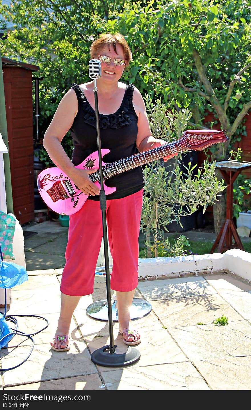 Photo of a woman playing her pink air guitar with a 1950's microphone. Photo of a woman playing her pink air guitar with a 1950's microphone.