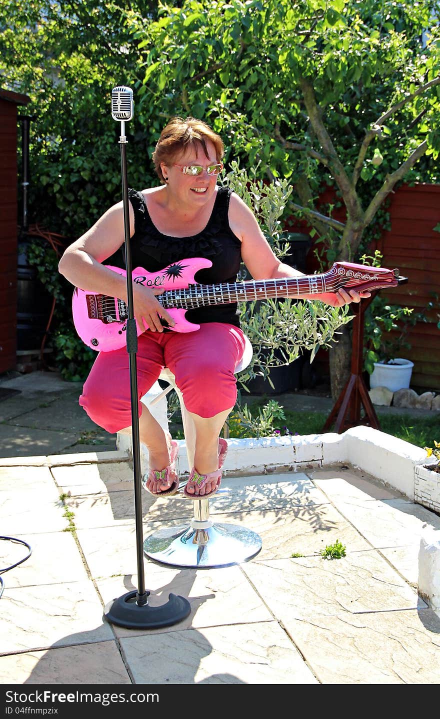 Photo of a woman seated having fun singing and playing a pink inflatable guitar. Photo of a woman seated having fun singing and playing a pink inflatable guitar.