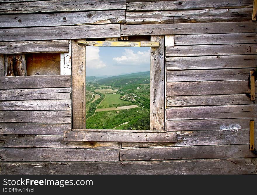 Landscape view through a window frame made in a wooden facade. Old wooden frame on the wall with a farmland view. Countryside with fields in a village - vintage farmhouse background.