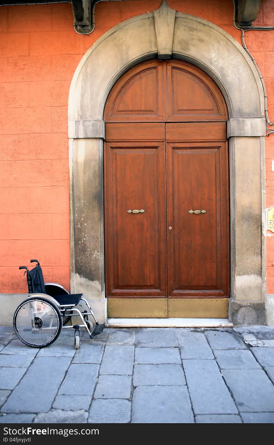 Urban scene. Empty wheelchair near old house with nice vintage wooden door. Urban scene. Empty wheelchair near old house with nice vintage wooden door