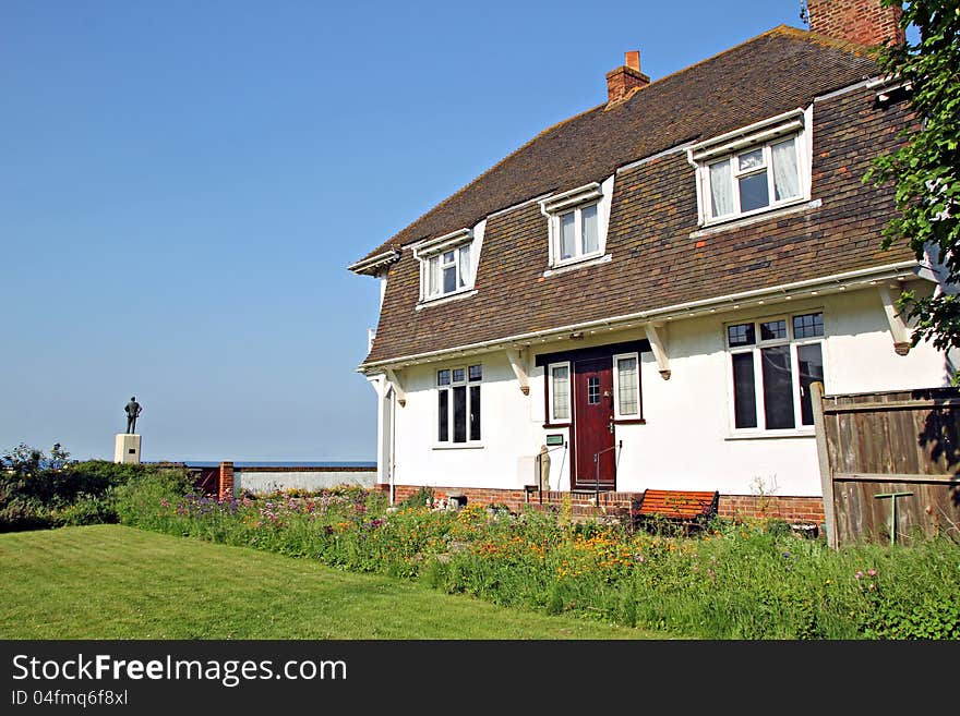 Photo of a beautiful cottage chalet style house by the sea with wild flowers growing in garden. Photo of a beautiful cottage chalet style house by the sea with wild flowers growing in garden.