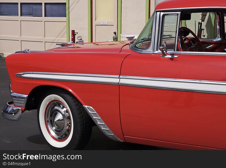 An old classic show car painted red at a historic gas station with a nice hood ornament. An old classic show car painted red at a historic gas station with a nice hood ornament