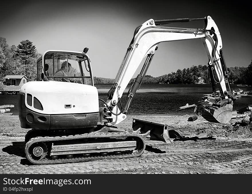 A man doing construction work in a backhoe on a beach in black & white. A man doing construction work in a backhoe on a beach in black & white.