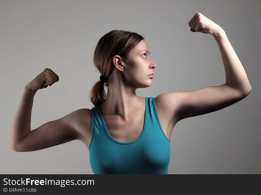 A young woman in blue tank top shows off her bicep. A young woman in blue tank top shows off her bicep.