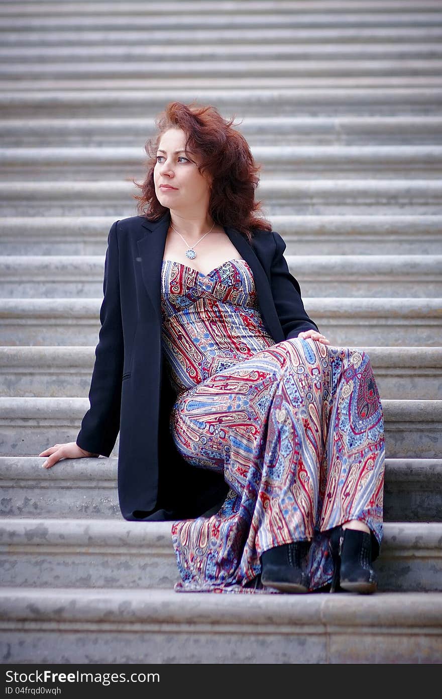 The beautiful woman in a jacket sits on steps