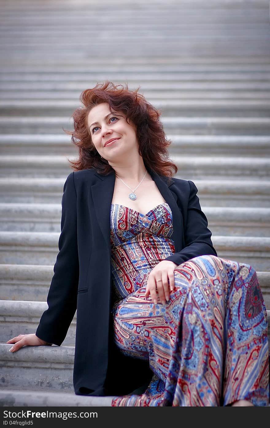 Portrait of the beautiful dreaming woman in a jacket sitting on steps