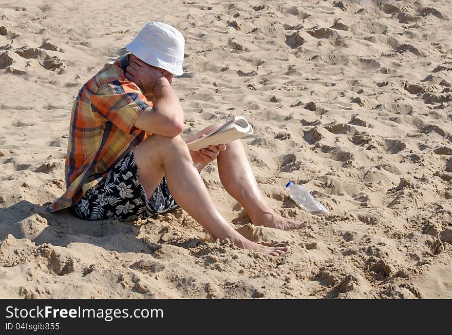 A man sits on the beach reading a magazine and keeping covered up from the hot sun. A man sits on the beach reading a magazine and keeping covered up from the hot sun