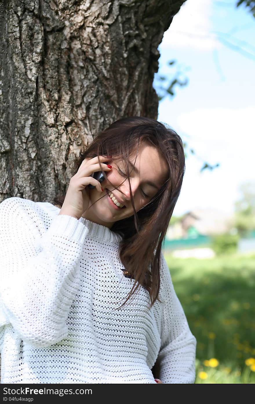 Smiling beauty teenage girl near tree talking on her mobile phone. Smiling beauty teenage girl near tree talking on her mobile phone