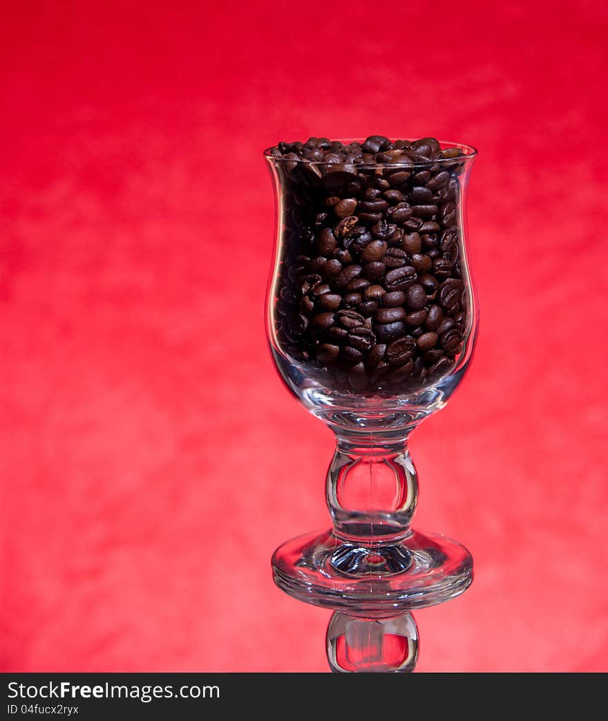 Grains of black roasted coffee in transparent cup  on red background. Grains of black roasted coffee in transparent cup  on red background