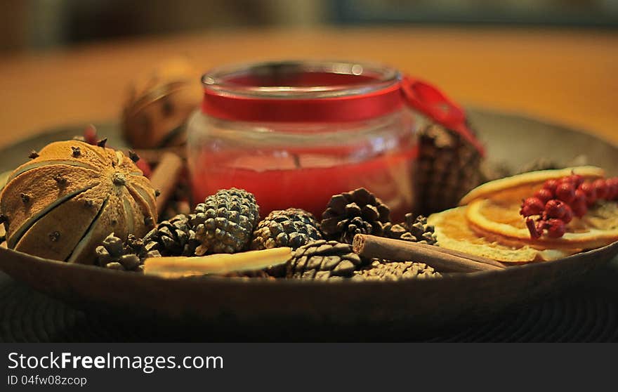 Potpourri bowl including orange and cloves, pine cones, berries, cinnamon, and a candle.