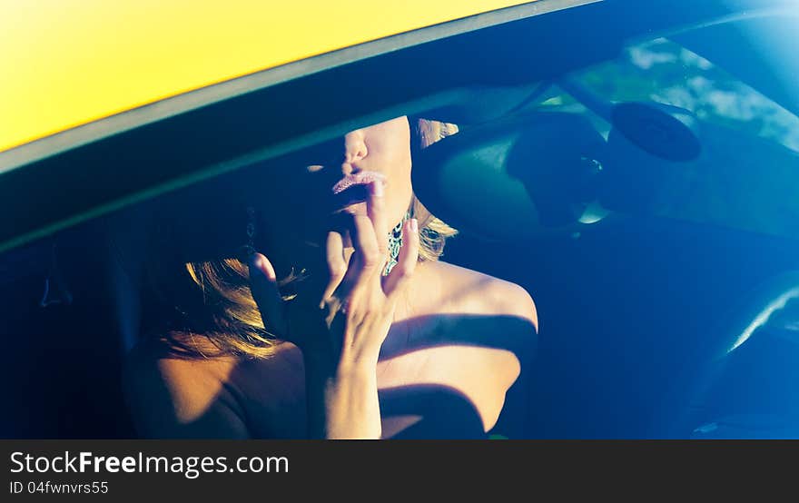 Through the glass picture a young woman in the car correcting her make-up. Through the glass picture a young woman in the car correcting her make-up