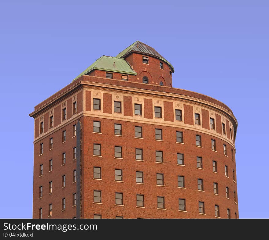 Upper stories of an old red brick building with a curved front and windows, isolated against the blue sky. Upper stories of an old red brick building with a curved front and windows, isolated against the blue sky.