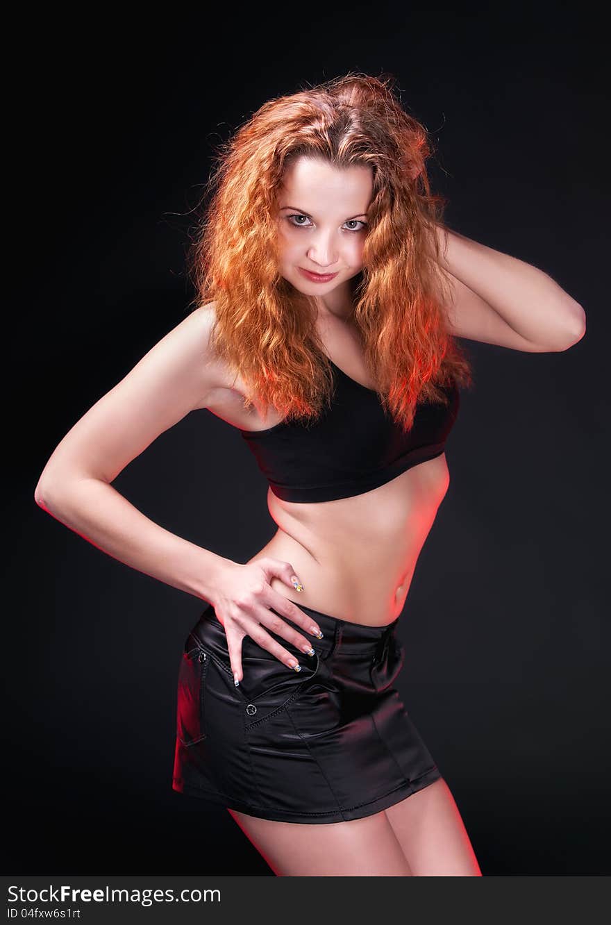 Portrait of a sexual redhead girl in a black bra and black leather skirt on a dark background