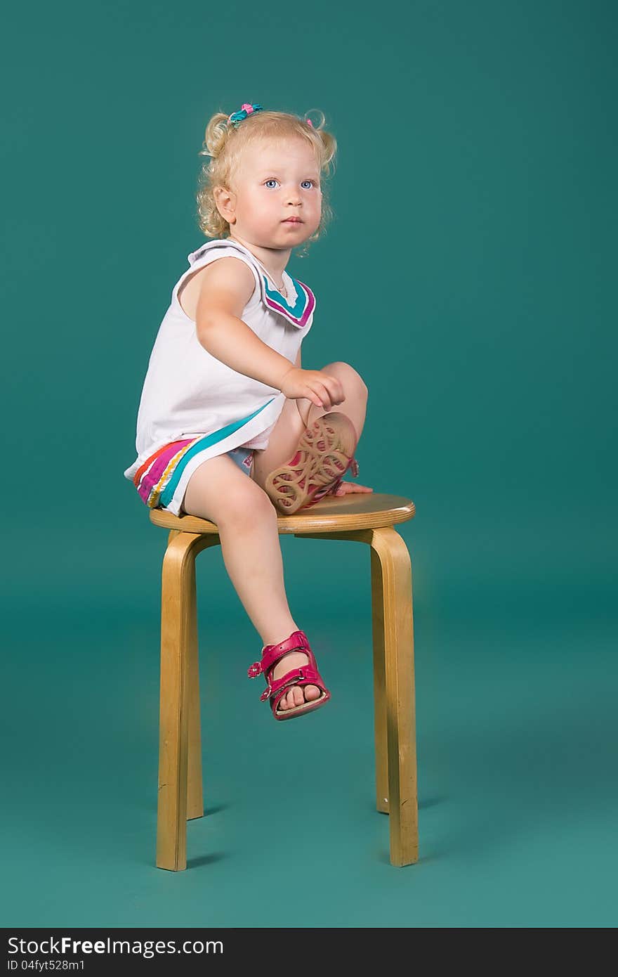 A girl in white dress sitting on a chair on the turquoise background in studio