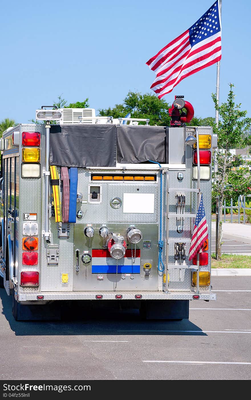 A shiny well kept fire truck with a United States flag mounted on it's bumper and a United States flag in the background. A shiny well kept fire truck with a United States flag mounted on it's bumper and a United States flag in the background