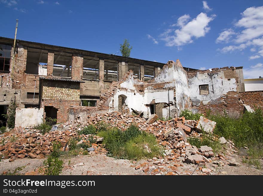 Complex of dilapidated buildings on a summer day, pile of bricks before the dilapidated building. Complex of dilapidated buildings on a summer day, pile of bricks before the dilapidated building