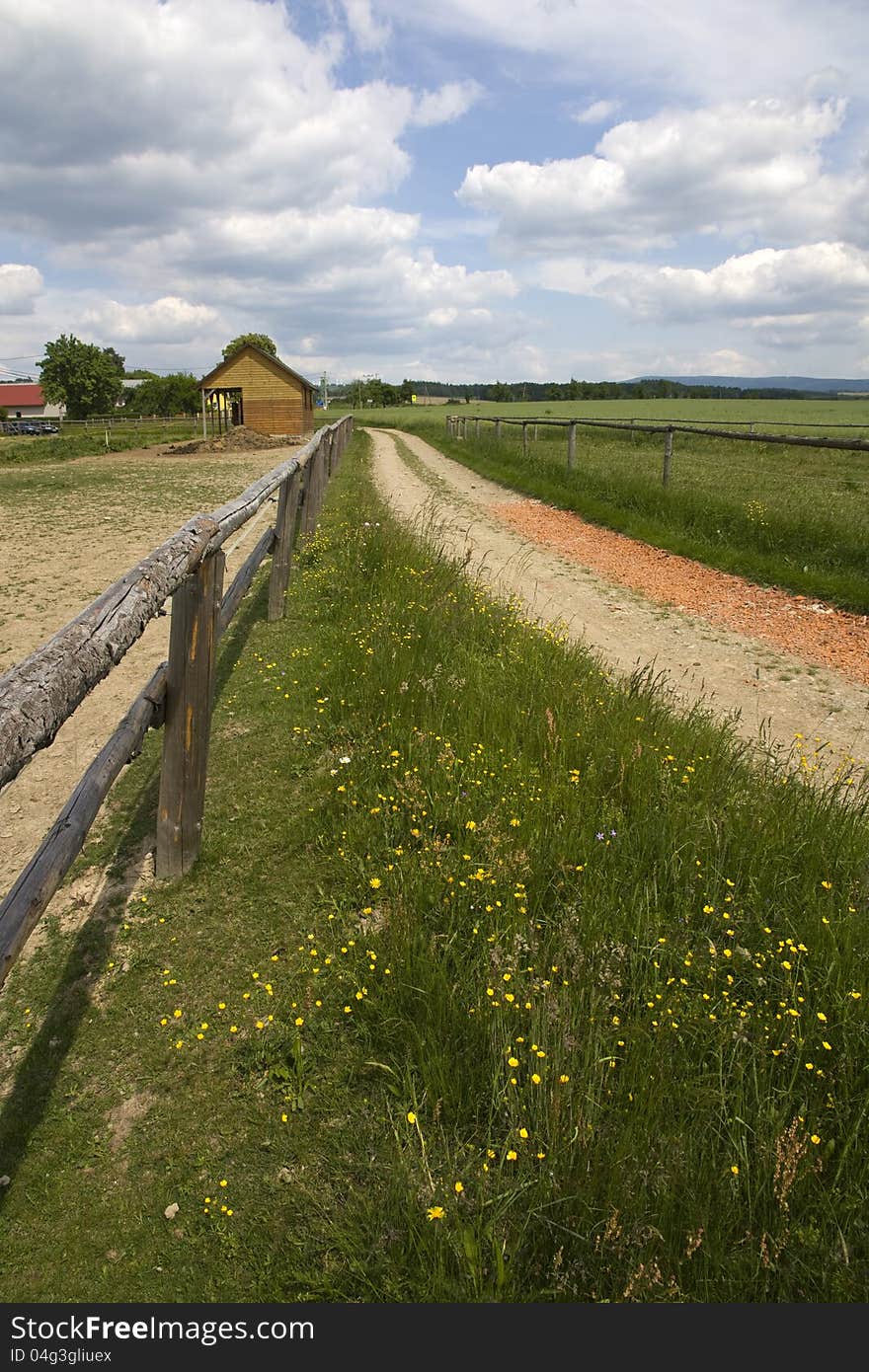 Dirt road with wooden fence in the country, rural landscape and ranch dwellings, summer landscape with a cloudy sky