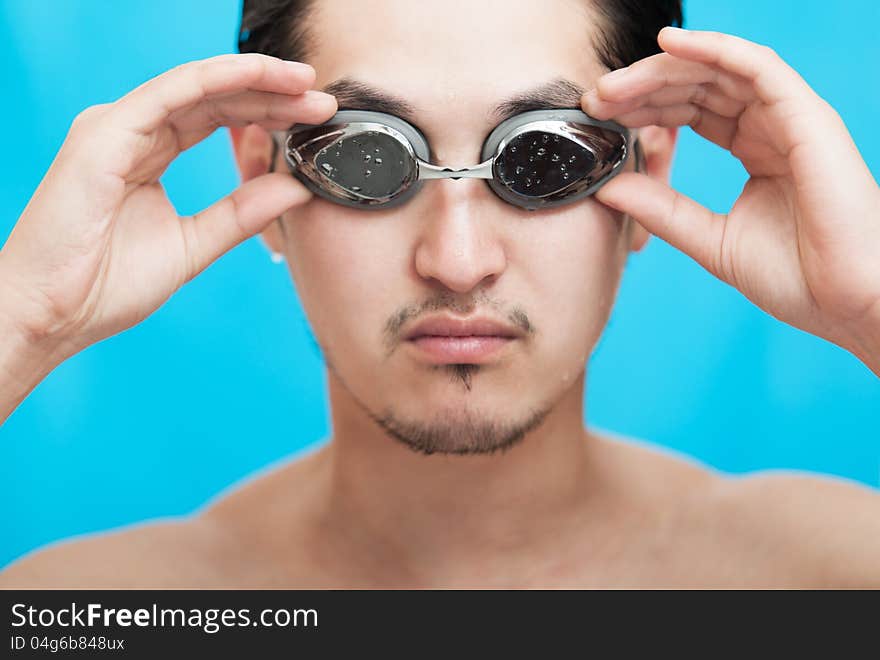 Portrait of the guy of asian appearance in swimming glasses on a blue background. Portrait of the guy of asian appearance in swimming glasses on a blue background