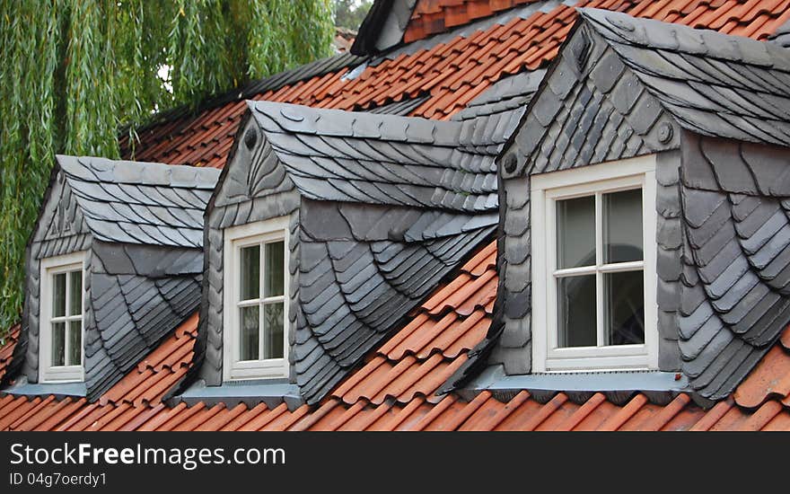 Three dormer windows with slates on red tile roof, characteristic of old houses in the Harzen capital, Goslar, Germany. Green willow in the back. Three dormer windows with slates on red tile roof, characteristic of old houses in the Harzen capital, Goslar, Germany. Green willow in the back