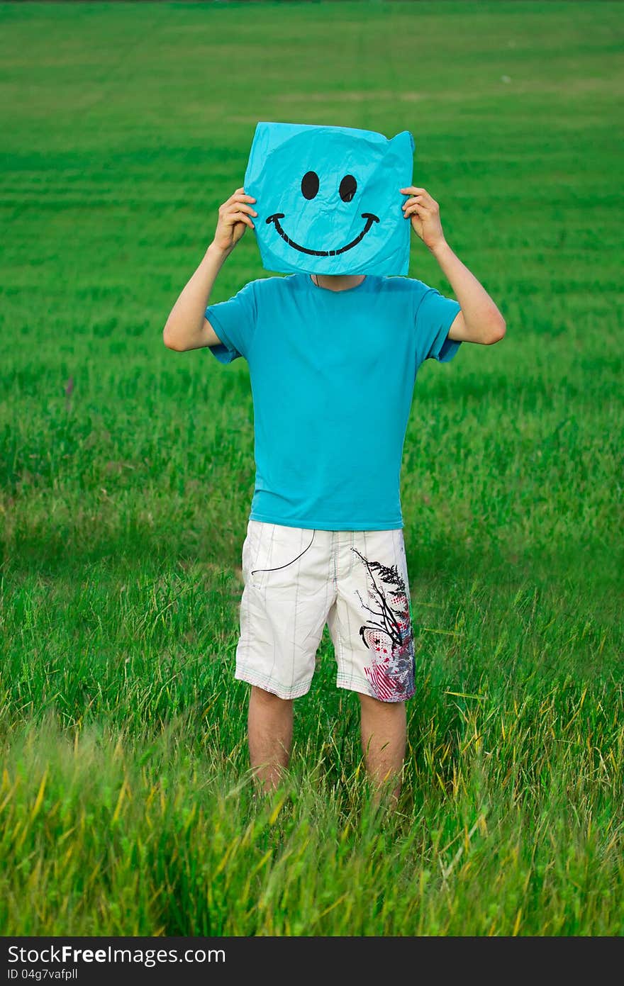 Happy young man in the summer field holds a rectangle with a painted smiley opposite face. Happy young man in the summer field holds a rectangle with a painted smiley opposite face