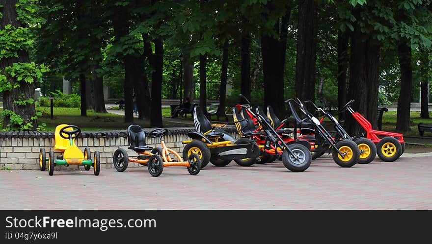 Many four wheeled bicycles on pavement on the park