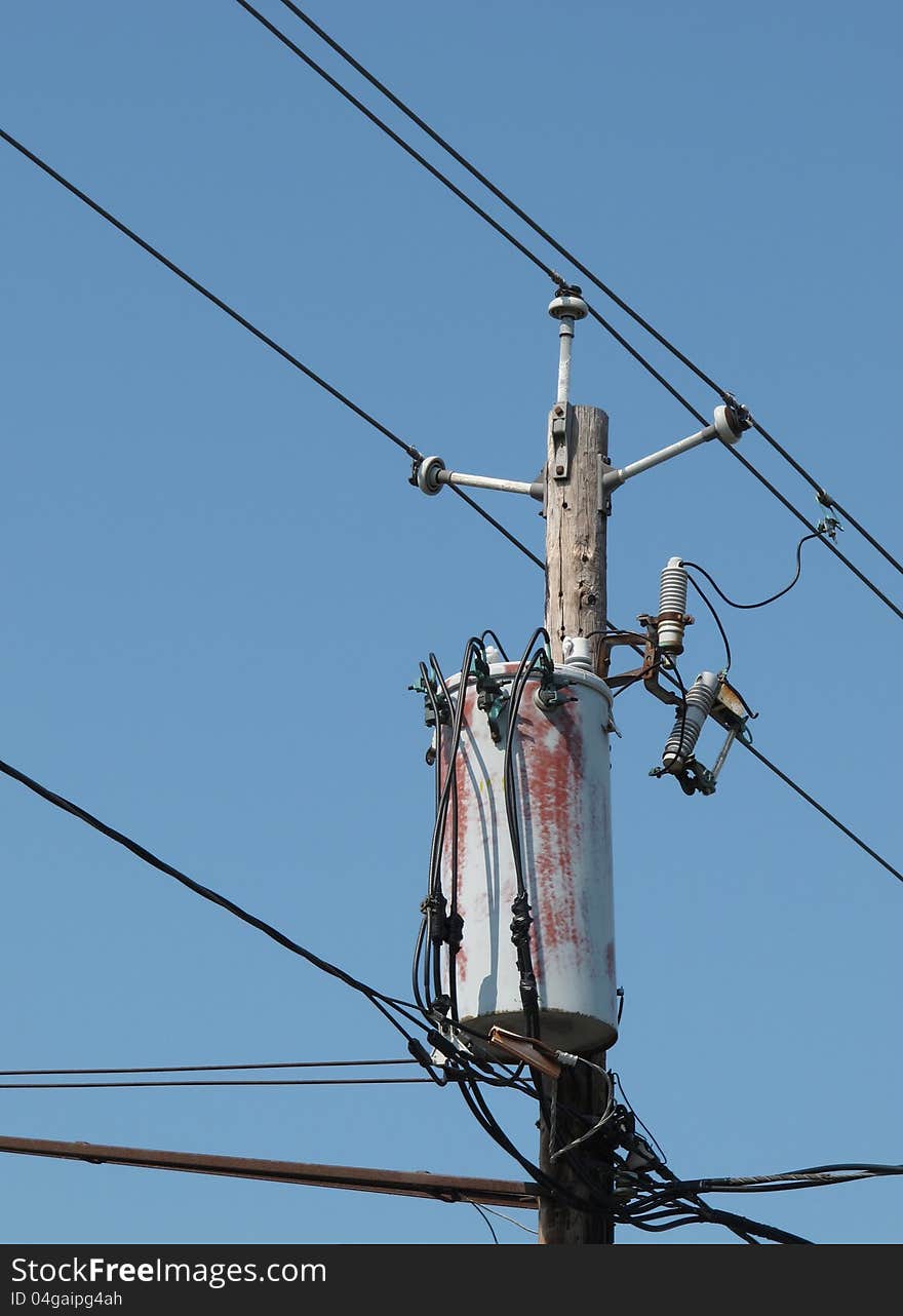 Top of an old wooden electrical pole with wires, connectors, and a transformer. Isolated against a blue sky. Top of an old wooden electrical pole with wires, connectors, and a transformer. Isolated against a blue sky.