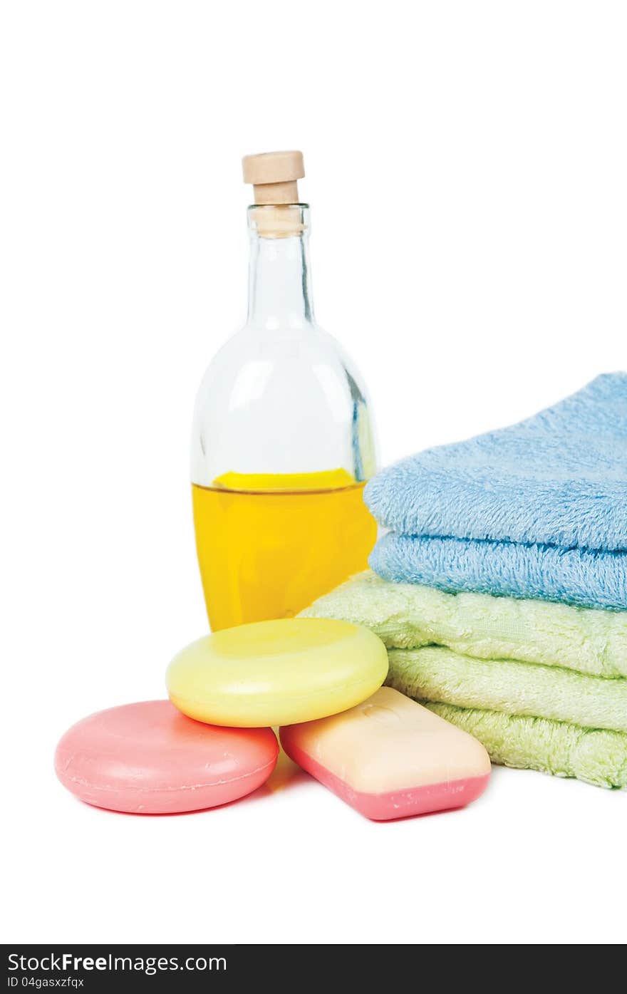 Three varicoloured bars of soap, two by a towel pile and massage oil. Three varicoloured bars of soap, two by a towel pile and massage oil