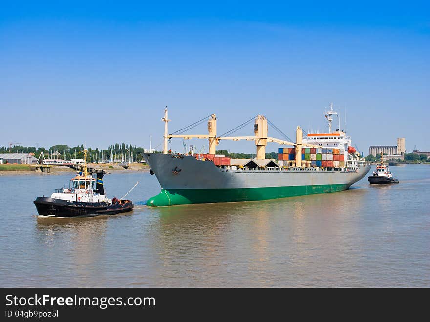 A large cargo ship is assisted by two tug boat on in the bow and the other in the stern. A large cargo ship is assisted by two tug boat on in the bow and the other in the stern