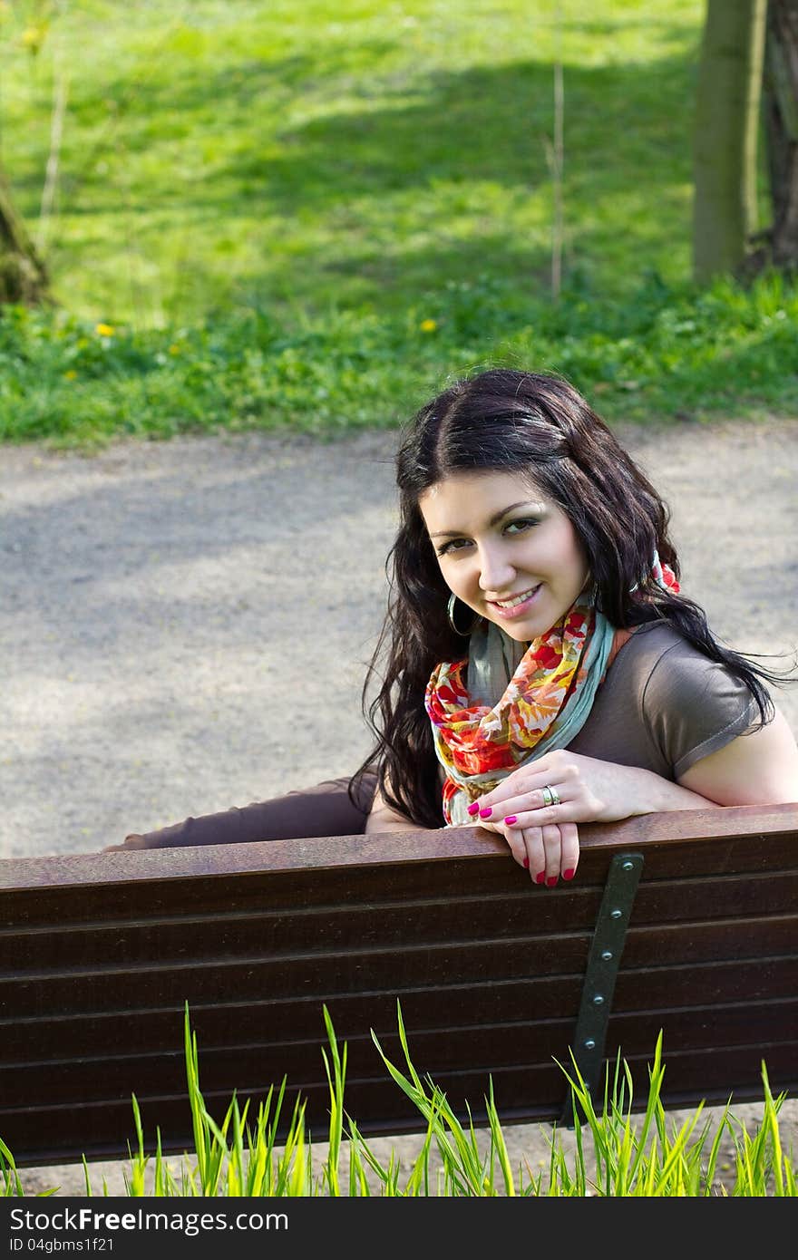 Beautiful young woman sitting on a bench at the park and smiling