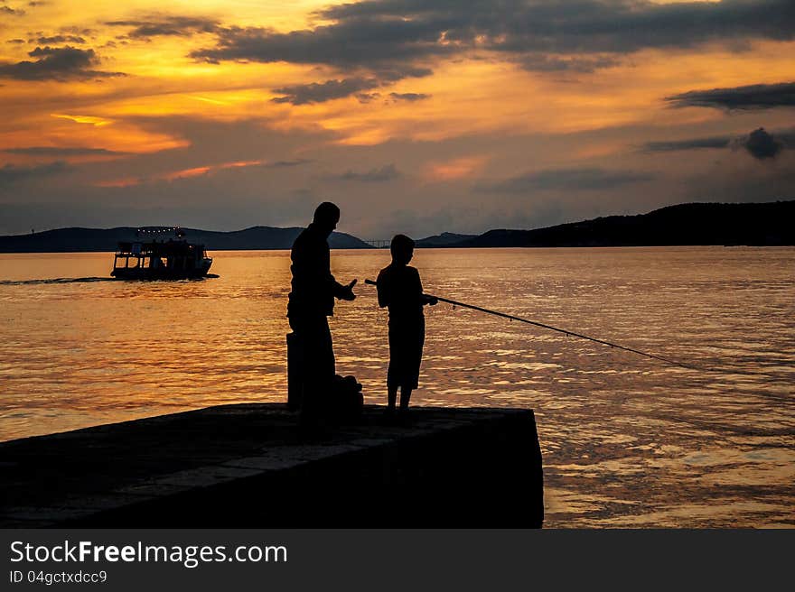 Silhouettes of father and his son fishing on the beach at sunset. Silhouettes of father and his son fishing on the beach at sunset