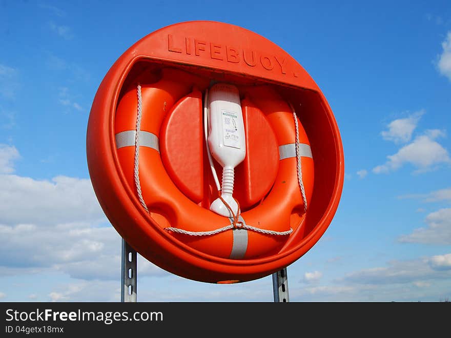 Rubber survival ring in vivid orange housing, blue sky in background. Rubber survival ring in vivid orange housing, blue sky in background