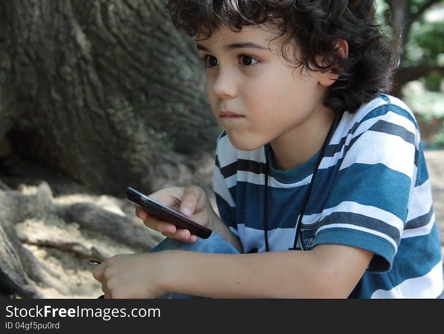 Beautiful curly child playing with cellphone sitting in the park. Beautiful curly child playing with cellphone sitting in the park