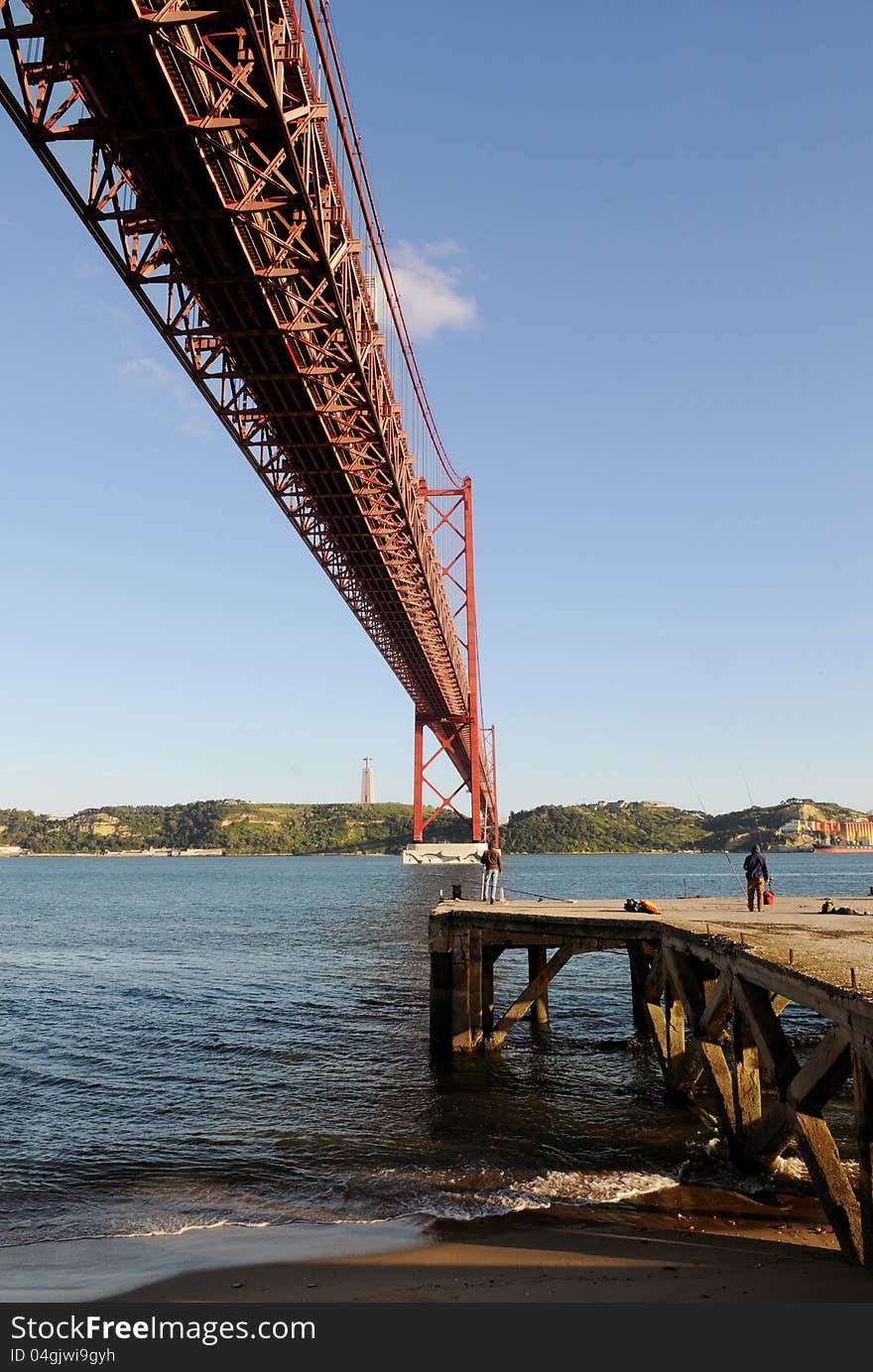 Fishing pier under the 25 de Abril Bridge (or 25th April Bridge), Lisbon, Portugal.