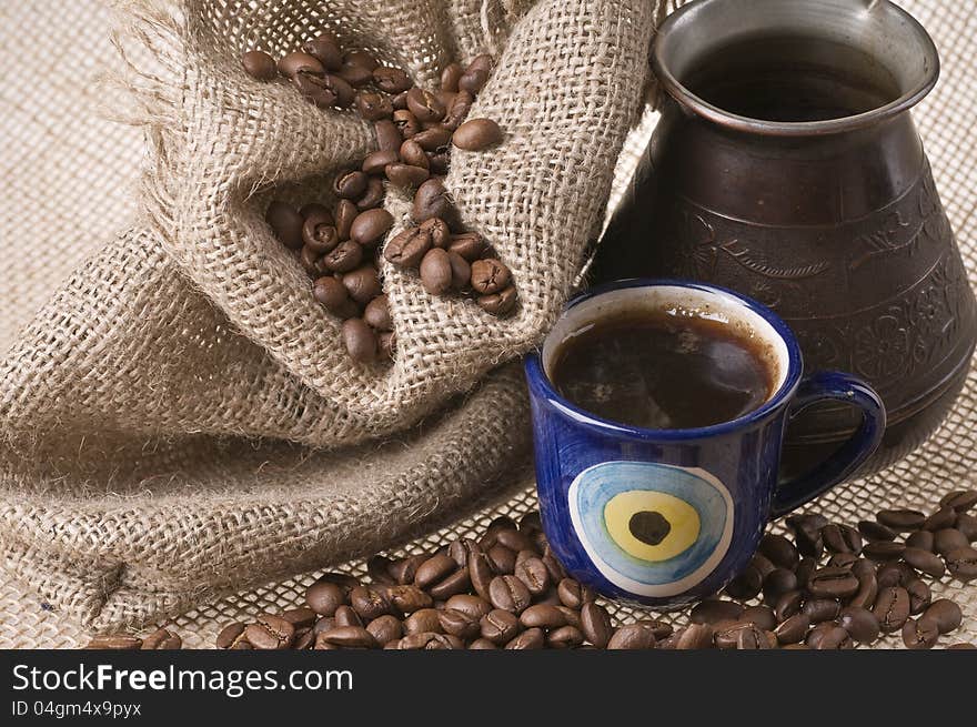 Cup of coffee with beans and sack over brown burlap background. Cup of coffee with beans and sack over brown burlap background