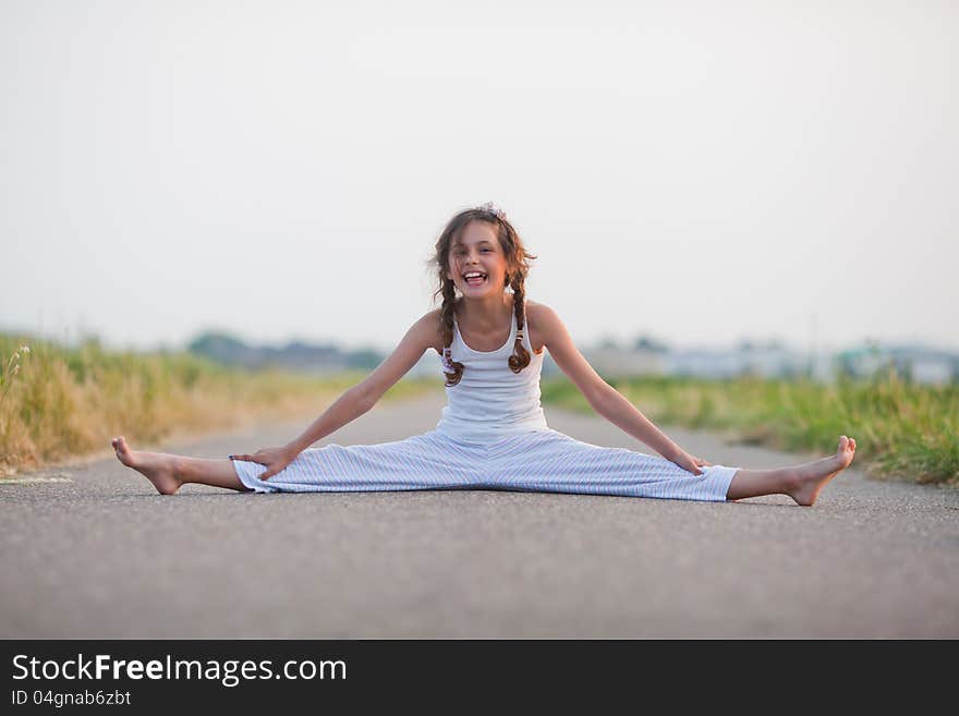 Cute young girl smiles and makes a split on a path. Cute young girl smiles and makes a split on a path