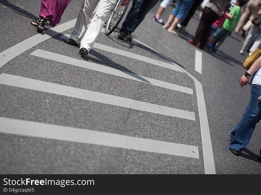 The picture shows the legs of a crowd of people that walks on the street during a street festival. The picture shows the legs of a crowd of people that walks on the street during a street festival